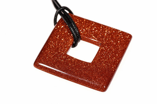 A square, donut-shaped pendant with a glittery orange-brown surface and a central hole, attached to a black cord against a white background.