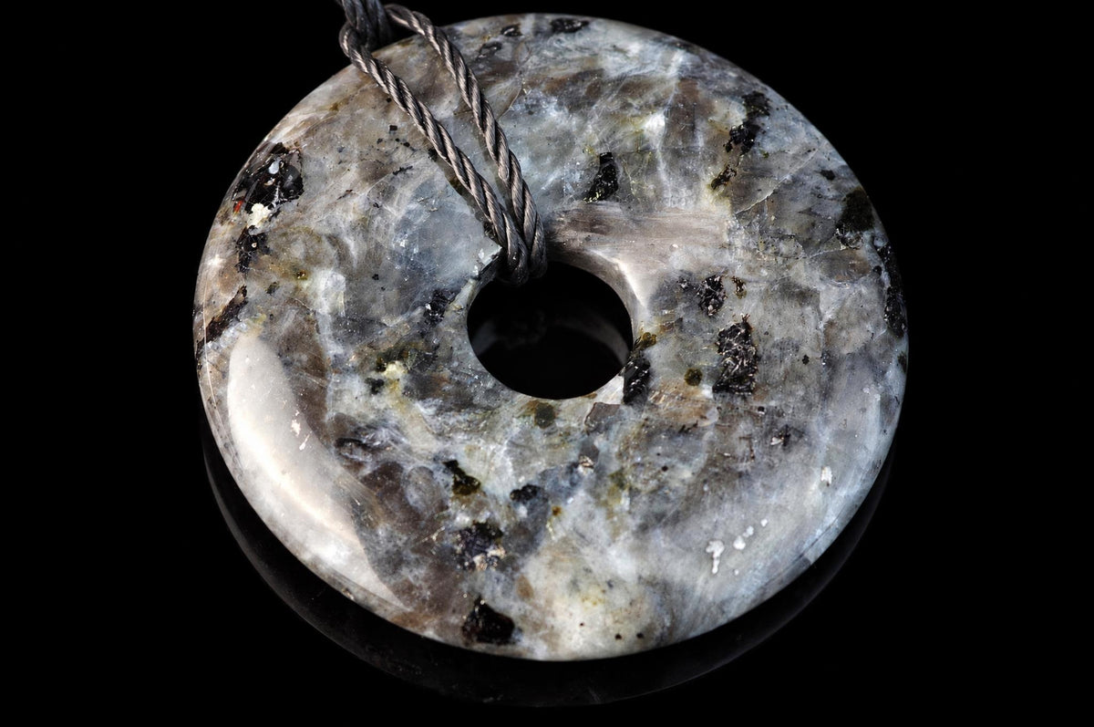A polished, donut-shaped pendant with a swirled grey, white and black stone pattern on a dark surface.