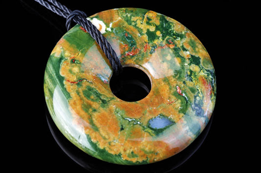 A polished, donut-shaped pendant with swirling green, orange, and white patterns on a dark surface.