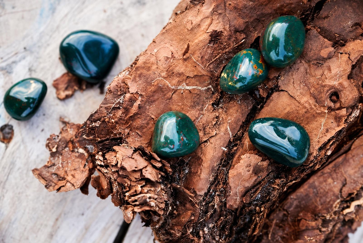 Polished dark green stones with orange specks rest on a rough brown wooden surface.