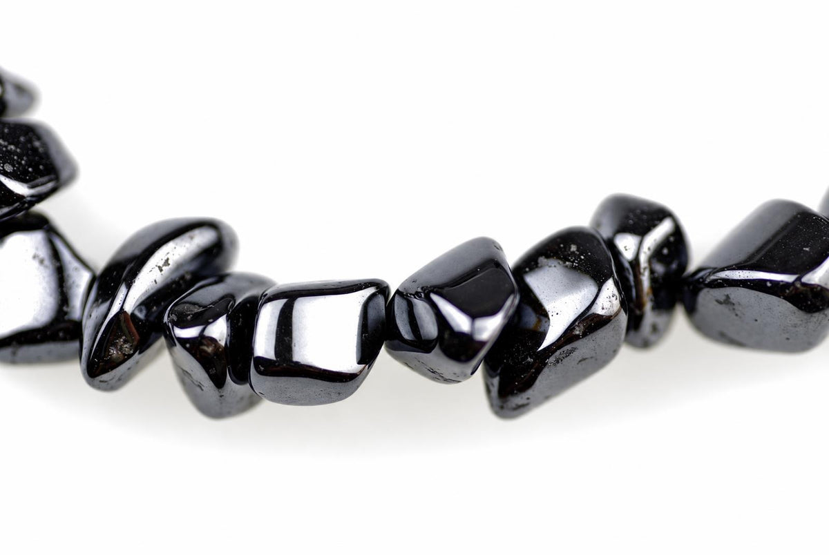 A strand of polished, irregular black beads with a metallic sheen lies on a white surface.