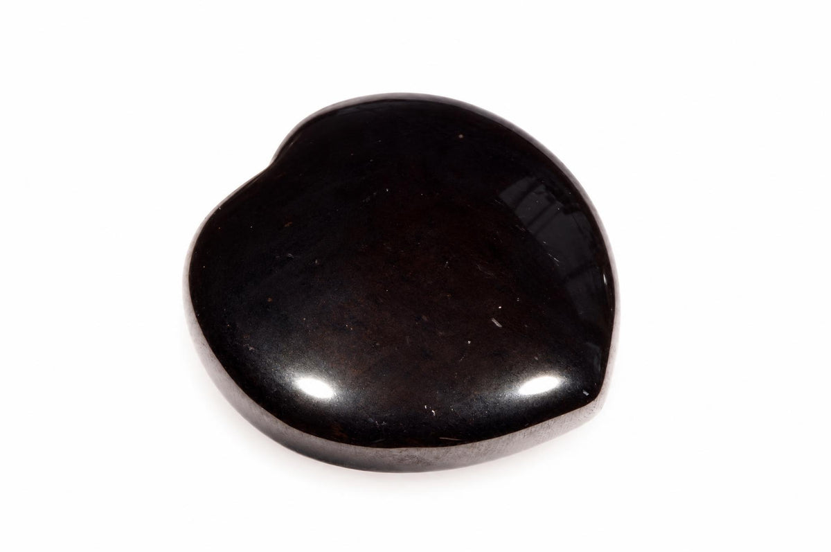 A polished, dark black stone with a smooth, heart-like shape rests on a white surface.