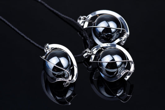 Three silver-toned pendants with black spheres and wire frames on dark cords, arranged on a reflective dark surface.