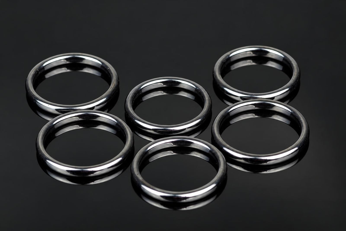 Six silver-toned rings with smooth, rounded edges arranged on a dark reflective surface.