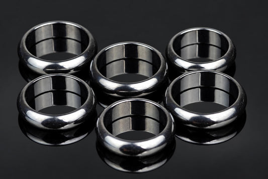 Six silver-toned rings with smooth, rounded bands arranged on a dark reflective surface.