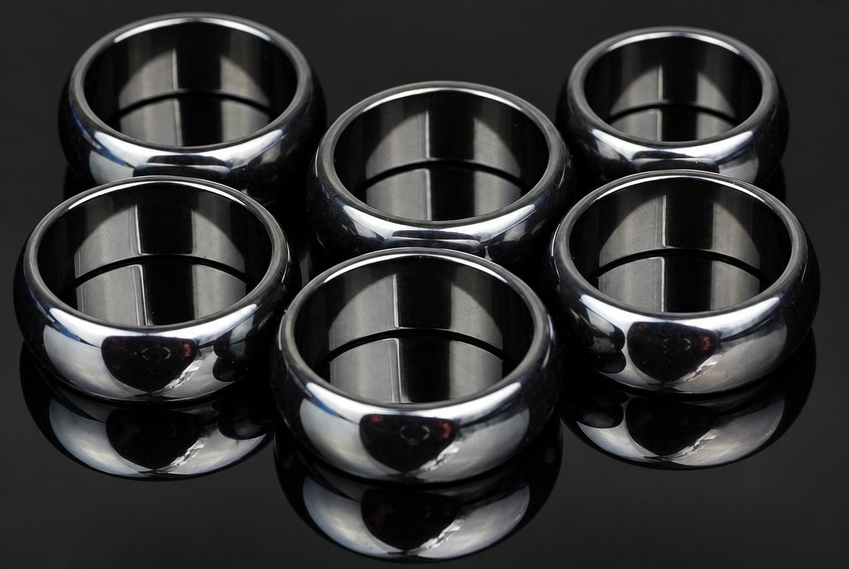 Six polished silver-toned rings arranged on a dark, reflective surface.