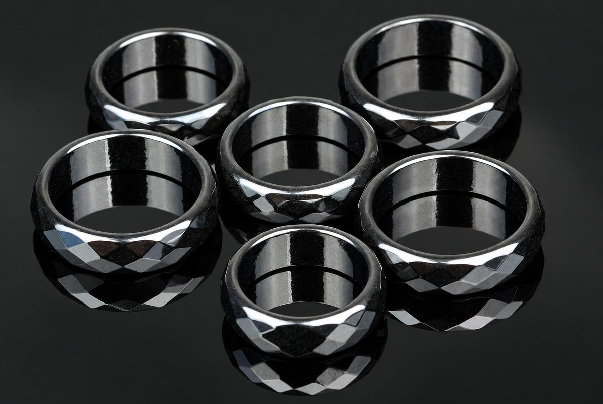 Six black faceted rings with silver-toned highlights arranged on a dark reflective surface.