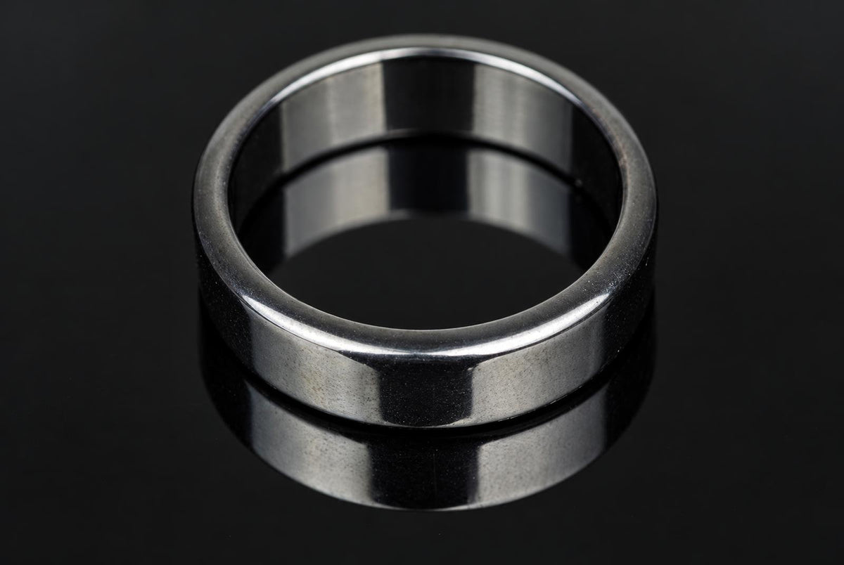 A silver-toned ring with a flat, polished band sits on a dark, reflective surface.
