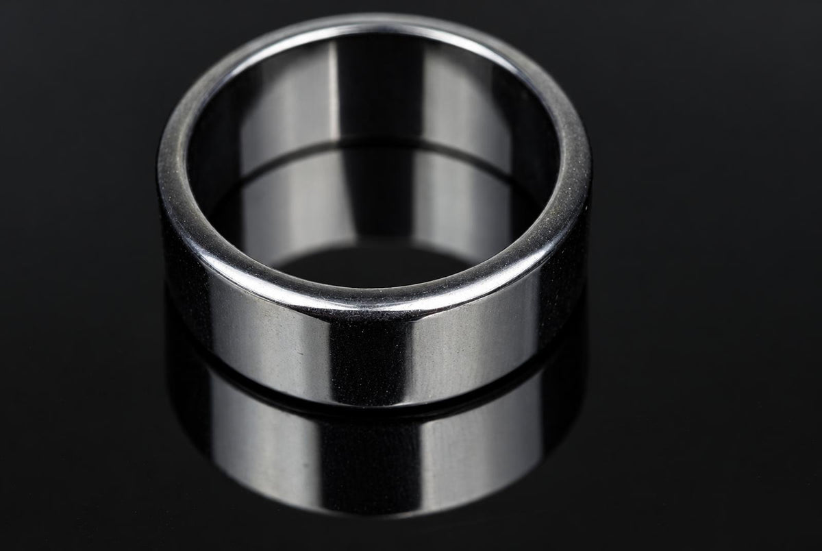 A silver-toned ring with a smooth, flat band sits on a dark surface.