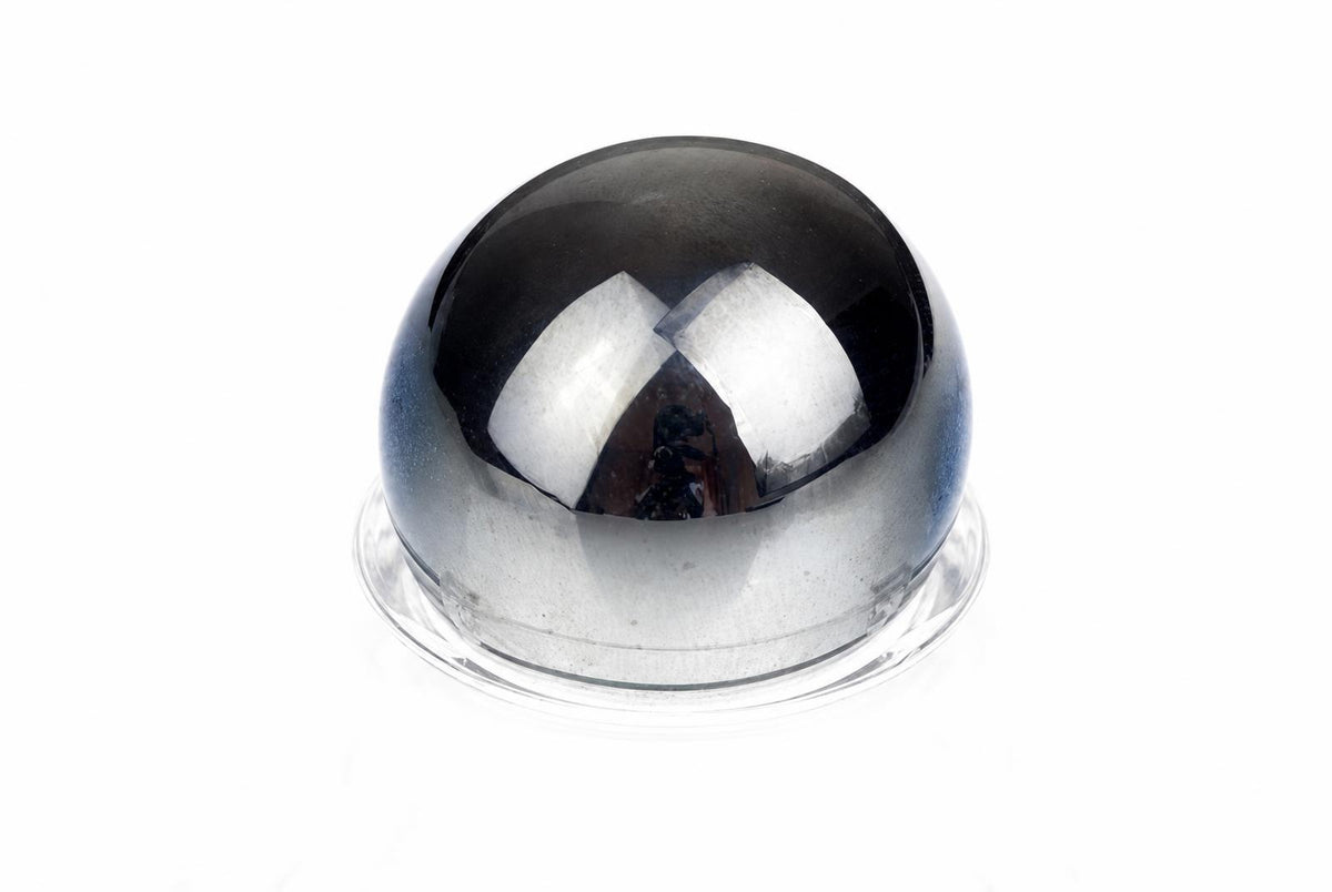 A polished, dark grey sphere sits on a clear base against a white background.