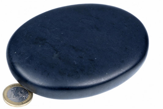 A smooth, dark blue oval massage stone rests on a white surface next to a one-euro coin for scale.