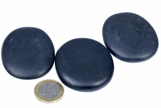 Three smooth, dark blue massage stones on a white surface with a one-euro coin for scale.