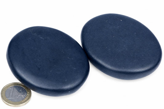 Two dark blue, smooth, oval massage stones on a white surface with a one-euro coin for scale.