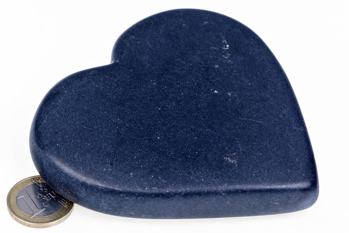 A dark blue, heart-shaped massage stone rests on a white surface next to a Euro coin for scale.