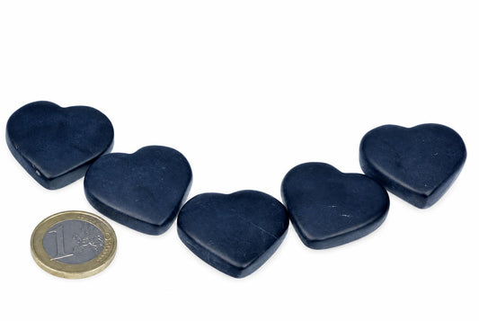 Five dark blue heart-shaped stones arranged on a white surface with a one-euro coin for scale.
