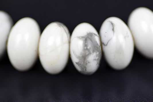 A row of white and grey marbled oval beads on a dark surface.
