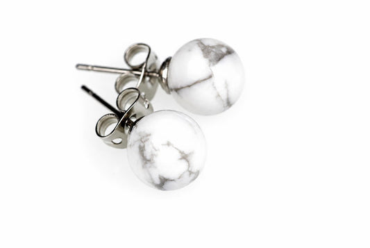 A pair of round white and grey patterned stud earrings with silver-toned posts on a pale surface.