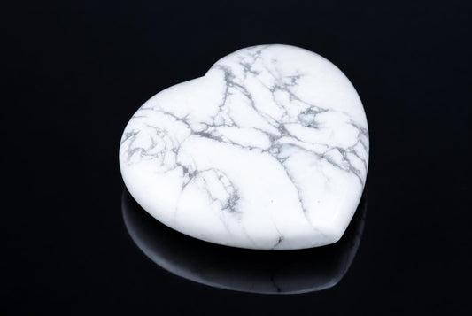 A polished, heart-shaped stone with white and grey veining rests on a dark surface.