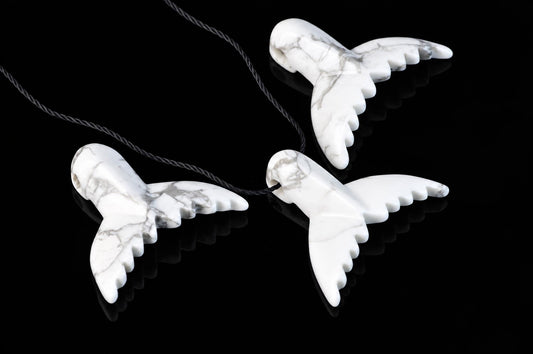 Three white dolphin-tail pendants with gray veining and black cords are arranged on a reflective black surface.