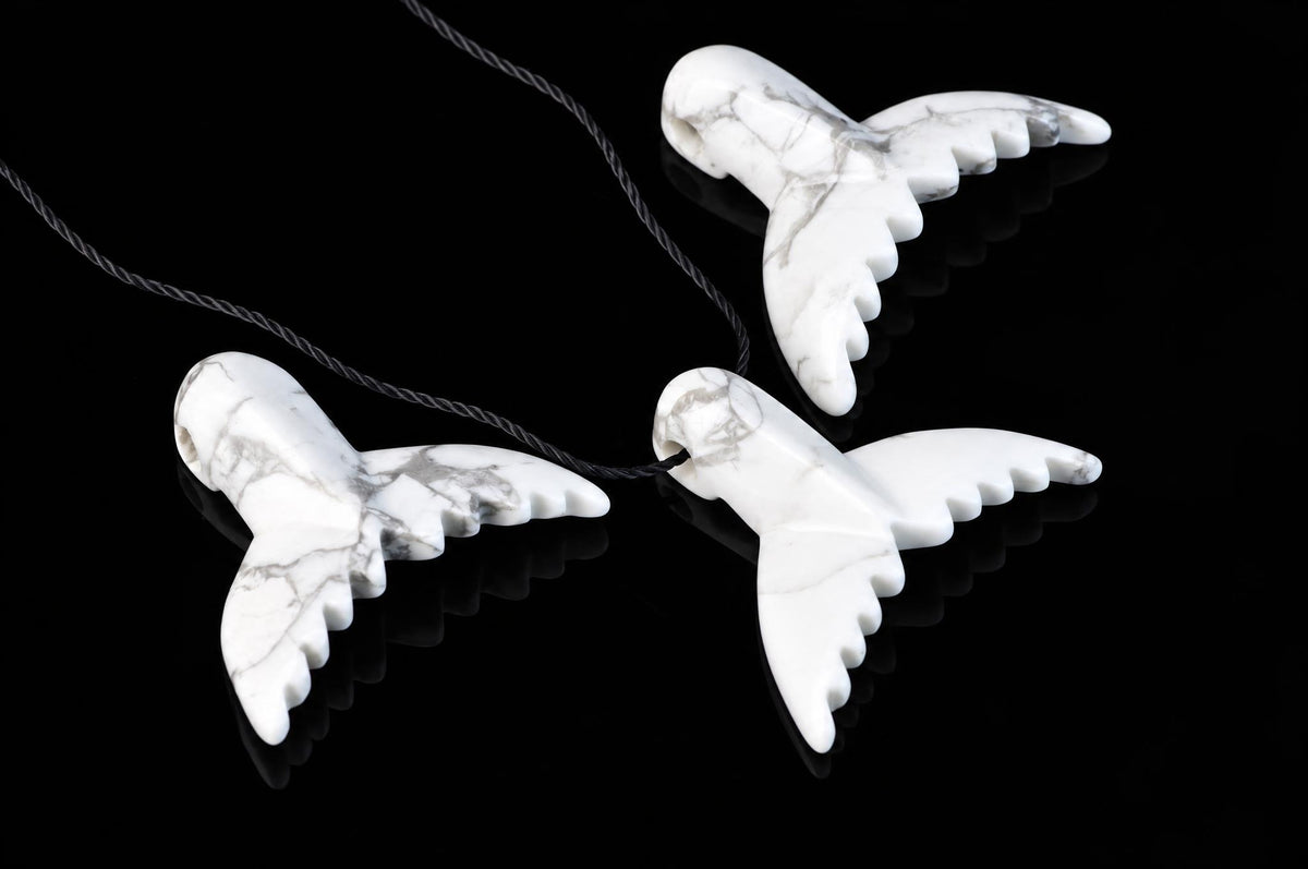 Three white dolphin-tail pendants with gray veining and black cords are arranged on a reflective black surface.