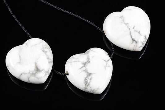 Three white heart-shaped pendants with grey veining hang from dark cords on a black reflective surface.