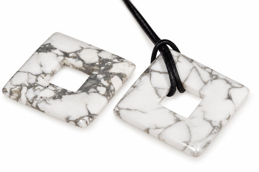 Two square, white-and-grey veined stone pendants with central cutouts; one has a black cord looped through its hole.