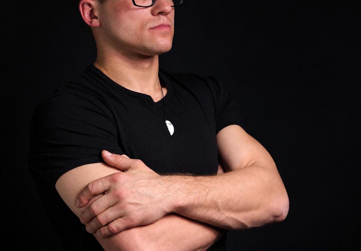 A man in a black t-shirt wears a white wing-shaped pendant on a dark surface.
