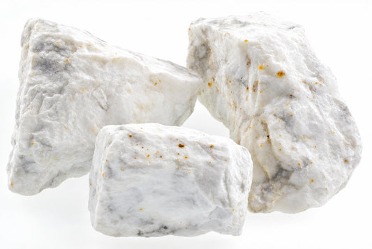 Three raw howlite stones with white, grey and brown speckles on a pale surface.