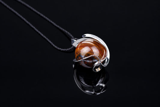 A silver-toned wire pendant holds a round, polished stone with brown and black patterns on a dark surface.