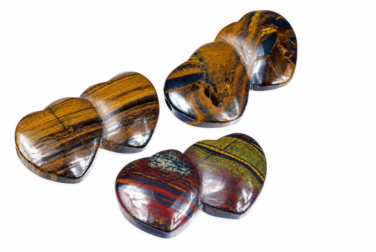Three polished, heart-shaped stones with striped patterns in brown, black, red and yellow on a white background.