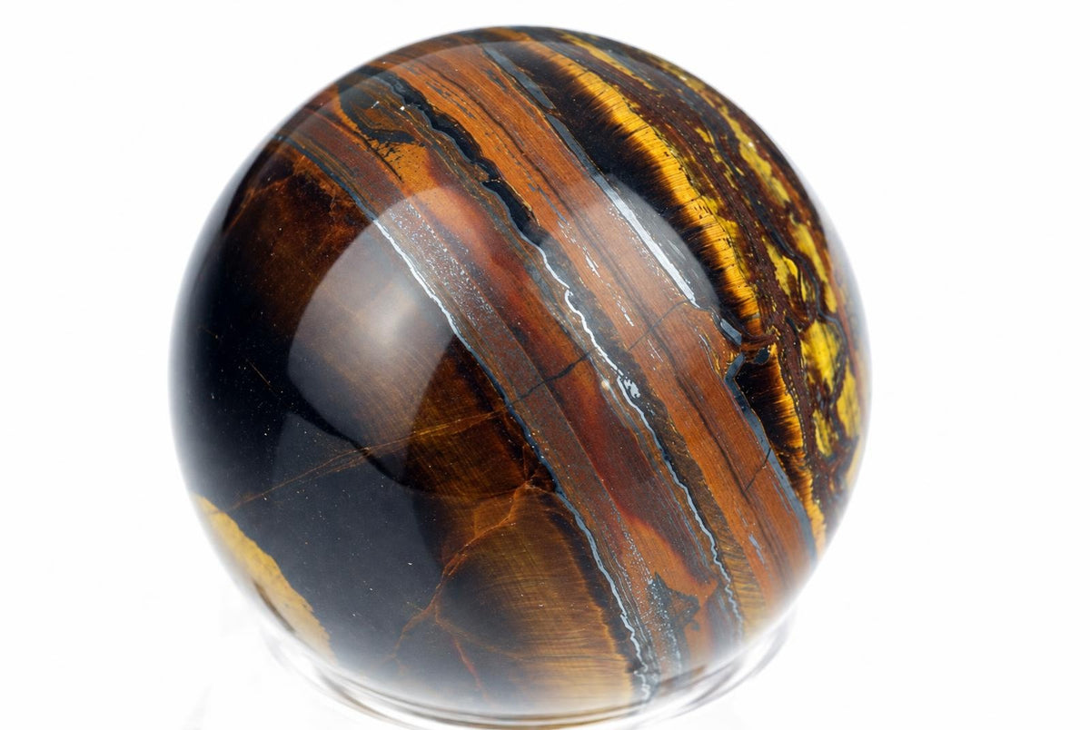 A polished sphere with swirling bands of black, brown, and yellow-orange on a white background.