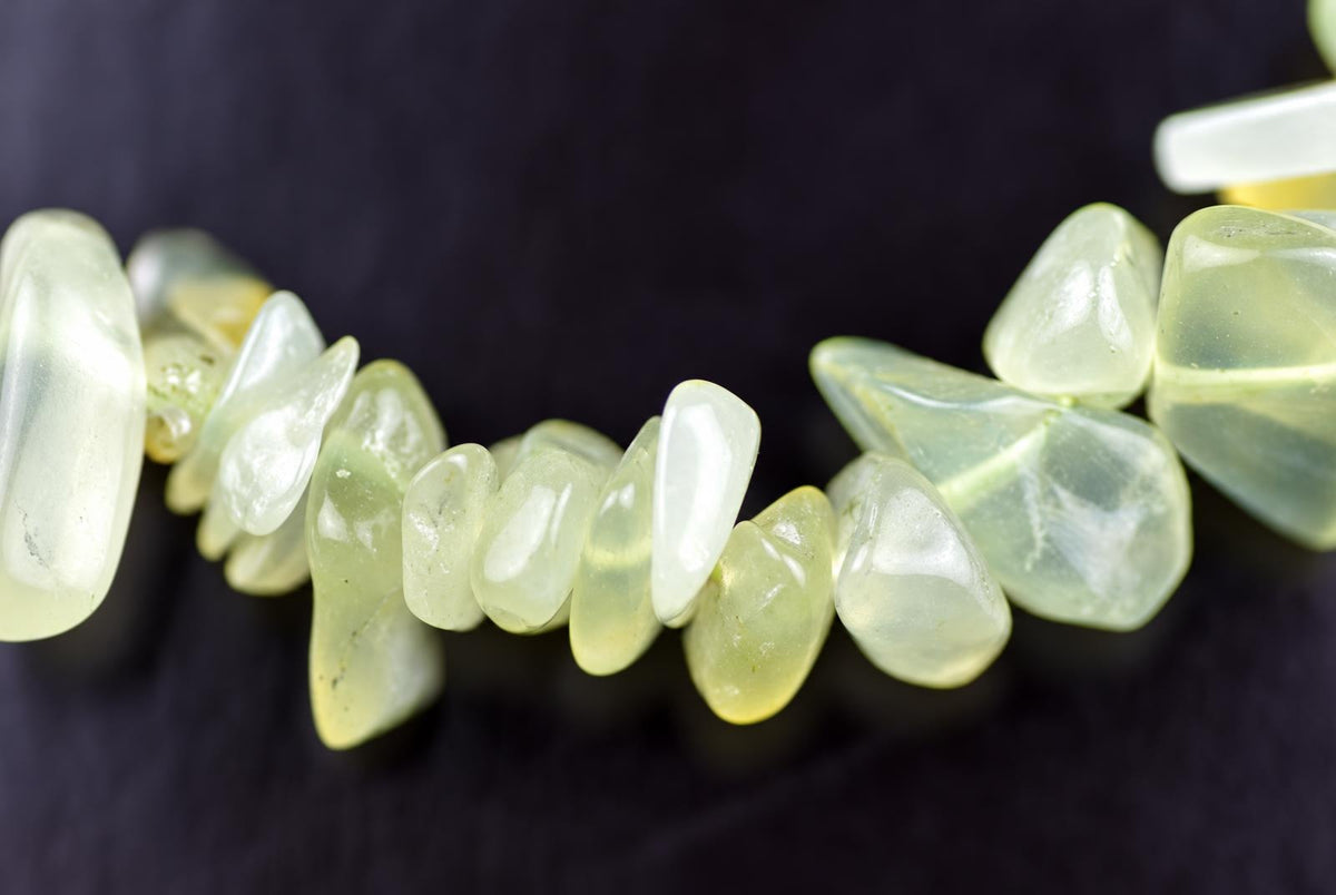 A strand of pale green and white polished chips, possibly jade, arranged on a dark surface.