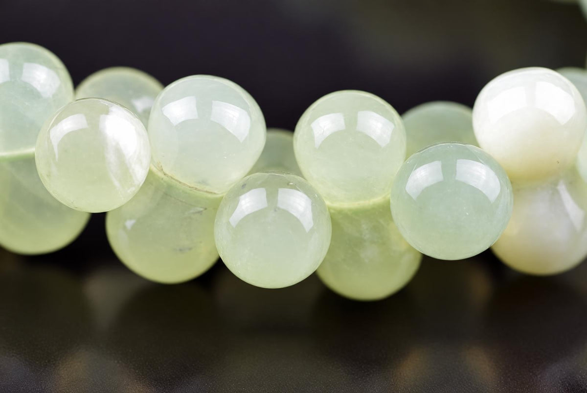 A close-up of a jade bracelet with round, pale green beads on a dark surface.