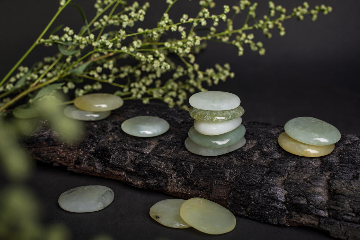 Several smooth, polished stones in pale green and yellow tones are arranged on a dark wooden surface with blurred greenery in the background.