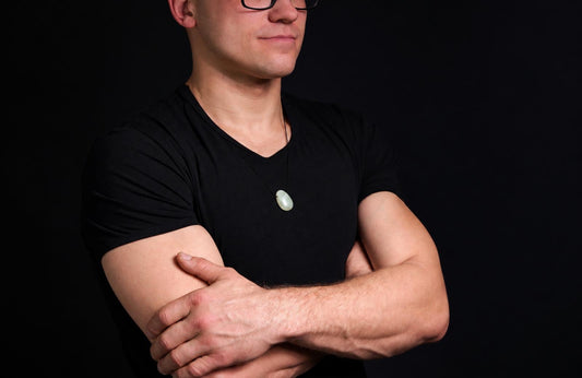 A man in a black shirt wears a light green jade pendant on a dark surface.