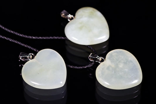 Three pale green heart pendants with metal loops and black cords are arranged on a reflective black surface.