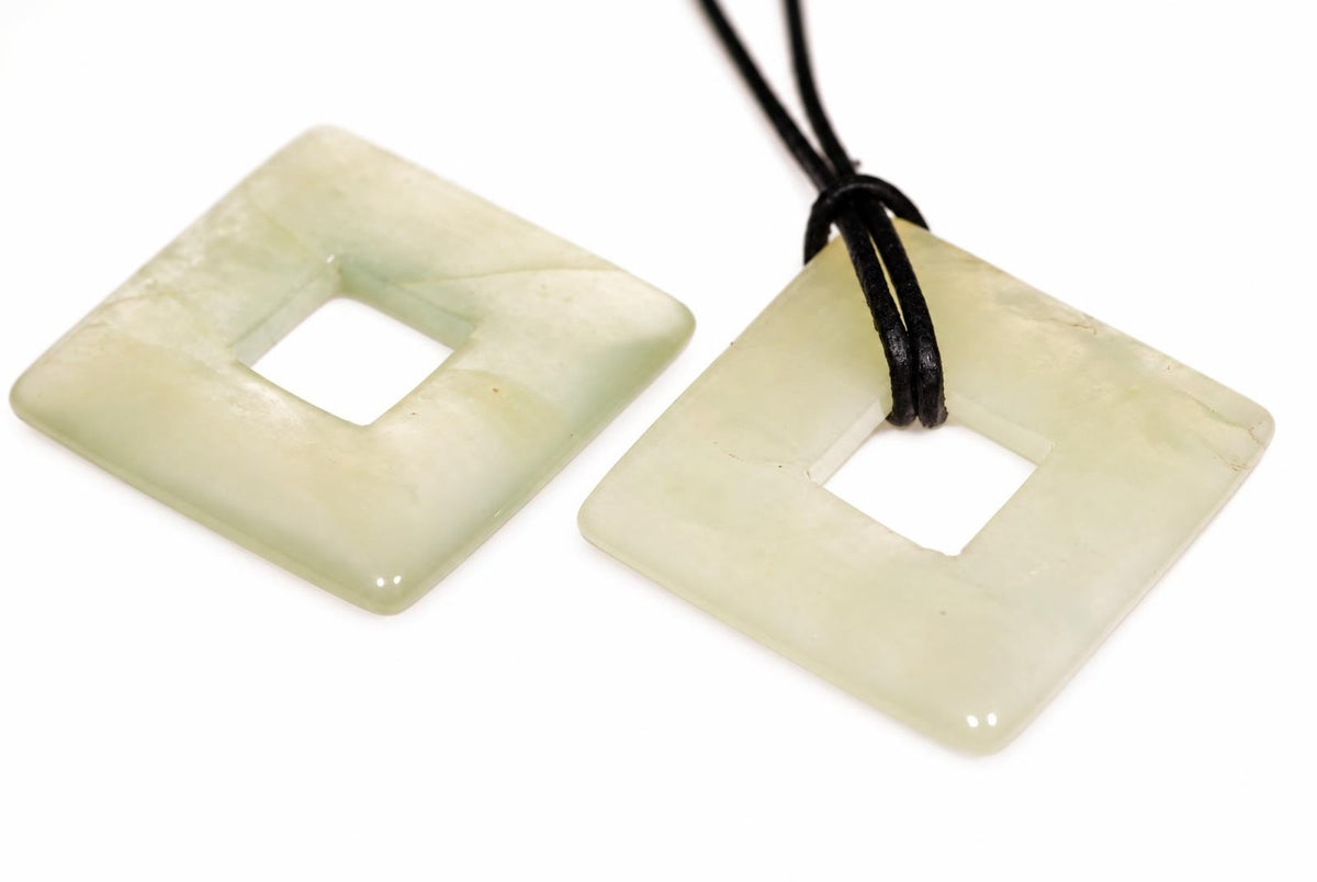 Two pale green square pendants with central holes; one has a black cord. They rest on a white surface.