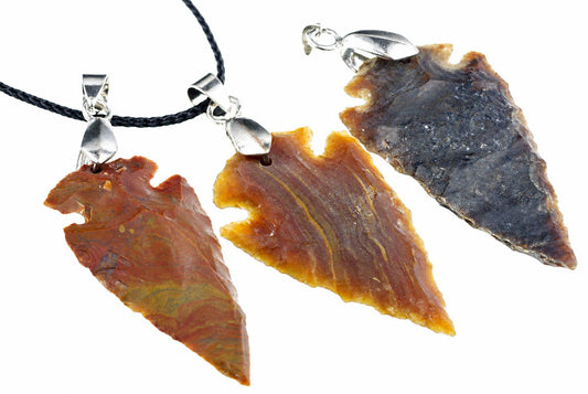 Three jasper arrowhead pendants show brown and orange tones with notched edges, suspended from black cords with silver-colored loops on white.