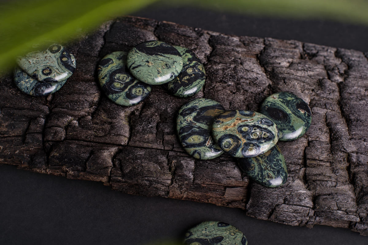 Several polished green and black patterned stones rest on a dark, textured wooden surface.