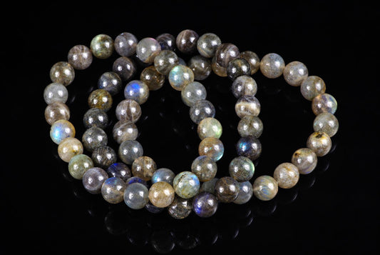 Overlapping bracelets of grey round beads with dark inclusions and blue-green flashes lie on black.