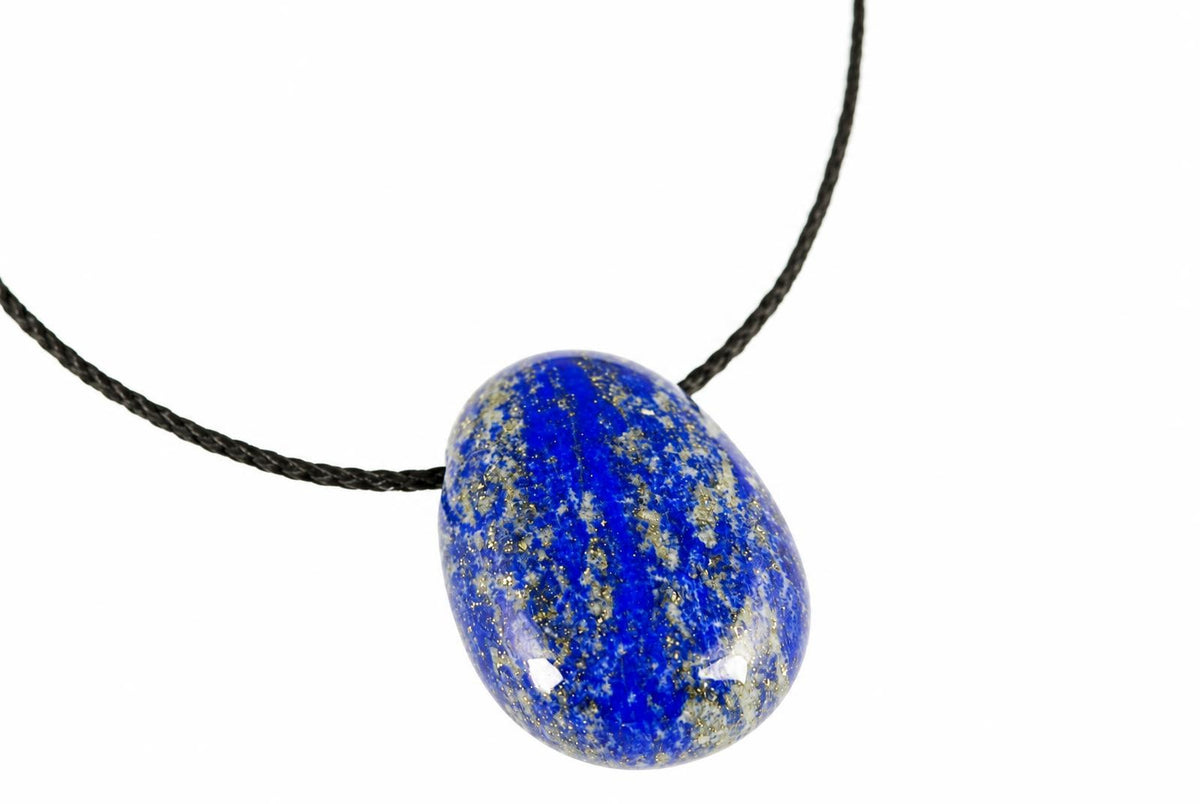 A polished deep blue lapis lazuli drop pendant shows pale and gold-colored flecks, suspended from a black cord on white.
