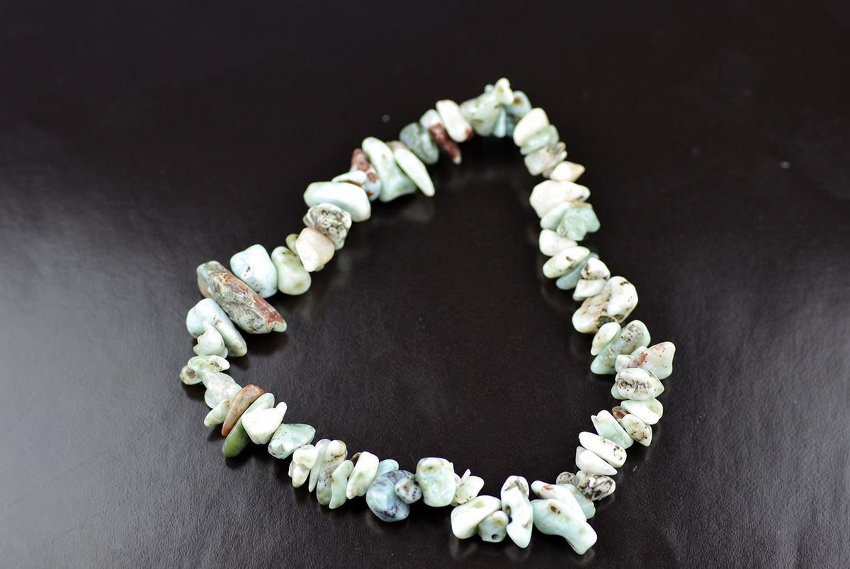A Larimar bracelet made of irregular chips in pale blue, white and brown tones on a dark surface.