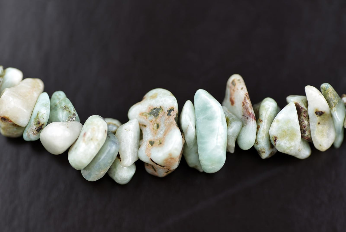 A strand of irregular Larimar chips in pale green, white and brown tones on a dark surface.