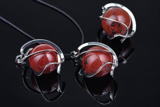 Three silver-toned wire pendants with round red spheres on a dark reflective surface.