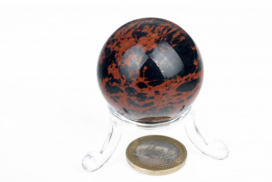 A polished sphere with black and reddish-brown patterns sits on a clear plastic stand against a white background.