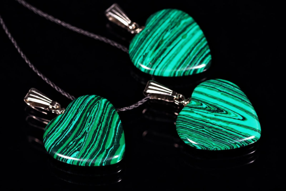 Three heart-shaped pendants with green and black striped patterns hang on cords against a dark surface.