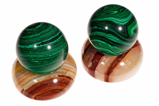 Two polished spheres on a white surface. The top sphere is green with dark swirls; the bottom sphere has brown, red and cream bands.