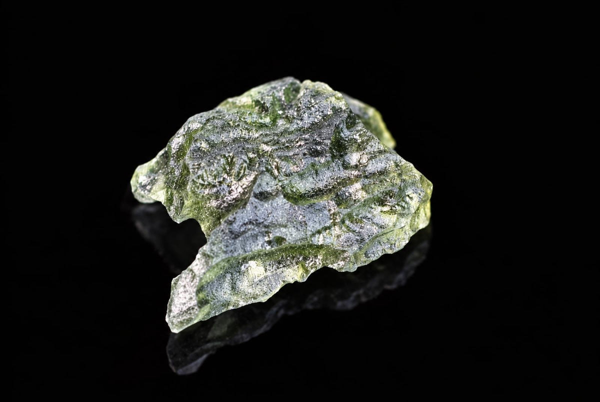 A green, glassy mineral specimen with a rough, irregular shape and silver-toned inclusions on a dark surface.