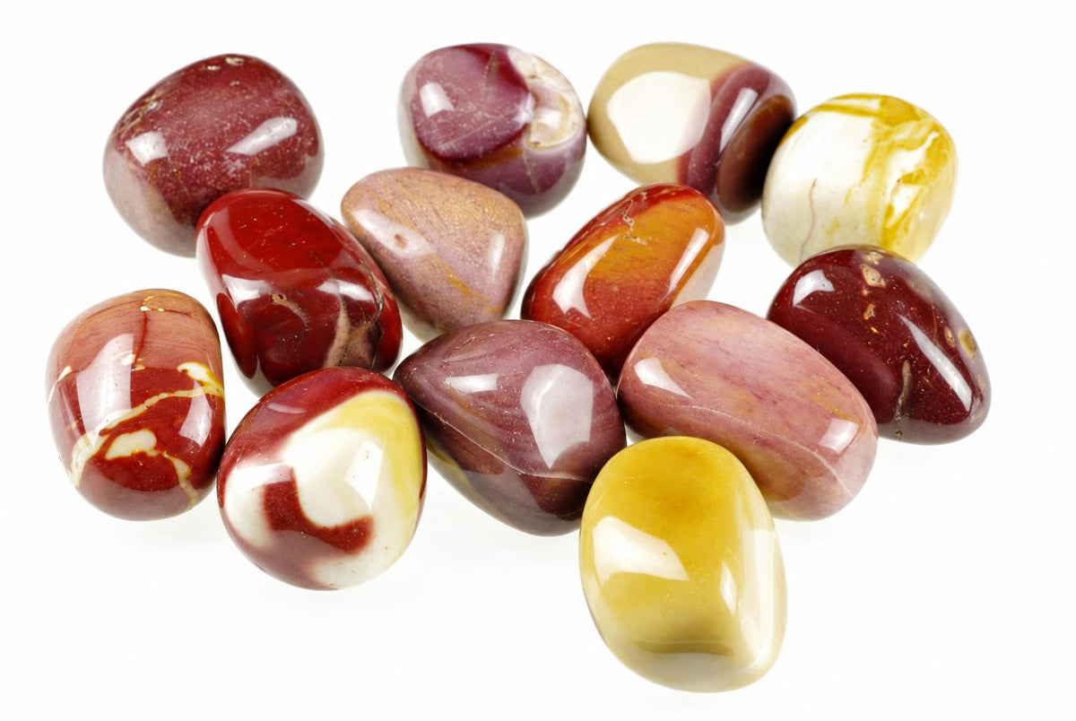 A collection of polished Mookaite Jasper stones in red, white, yellow and brown tones arranged on a pale surface.