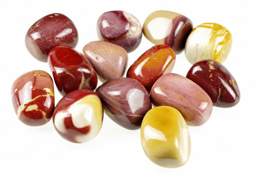 A collection of polished Mookaite Jasper stones in red, white, yellow and brown tones arranged on a pale surface.